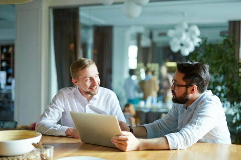 a couple of men sitting at a table with a laptop